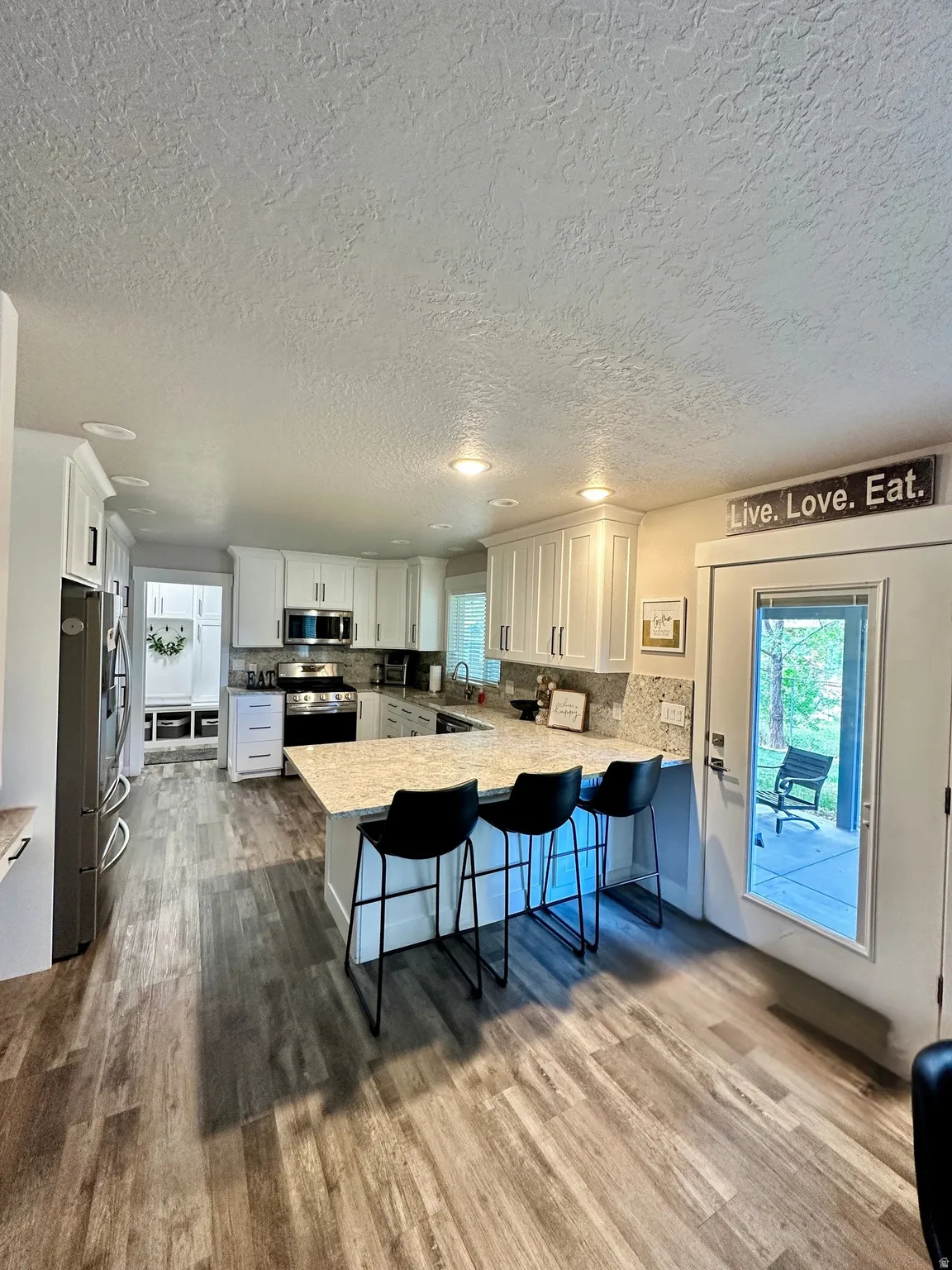 Spacious kitchen featuring wood-finish flooring, white cabinetry, recessed lighting, stainless steel appliances, and a central island with bar seating