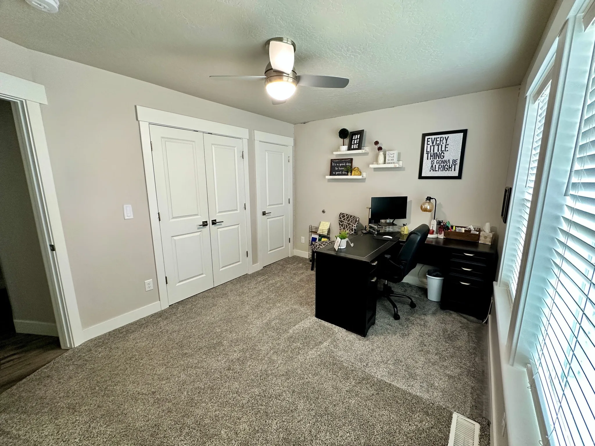Carpeted room featuring multiple windows with blinds, a ceiling fan with integrated lighting, and white paneled doors with dark hardware
