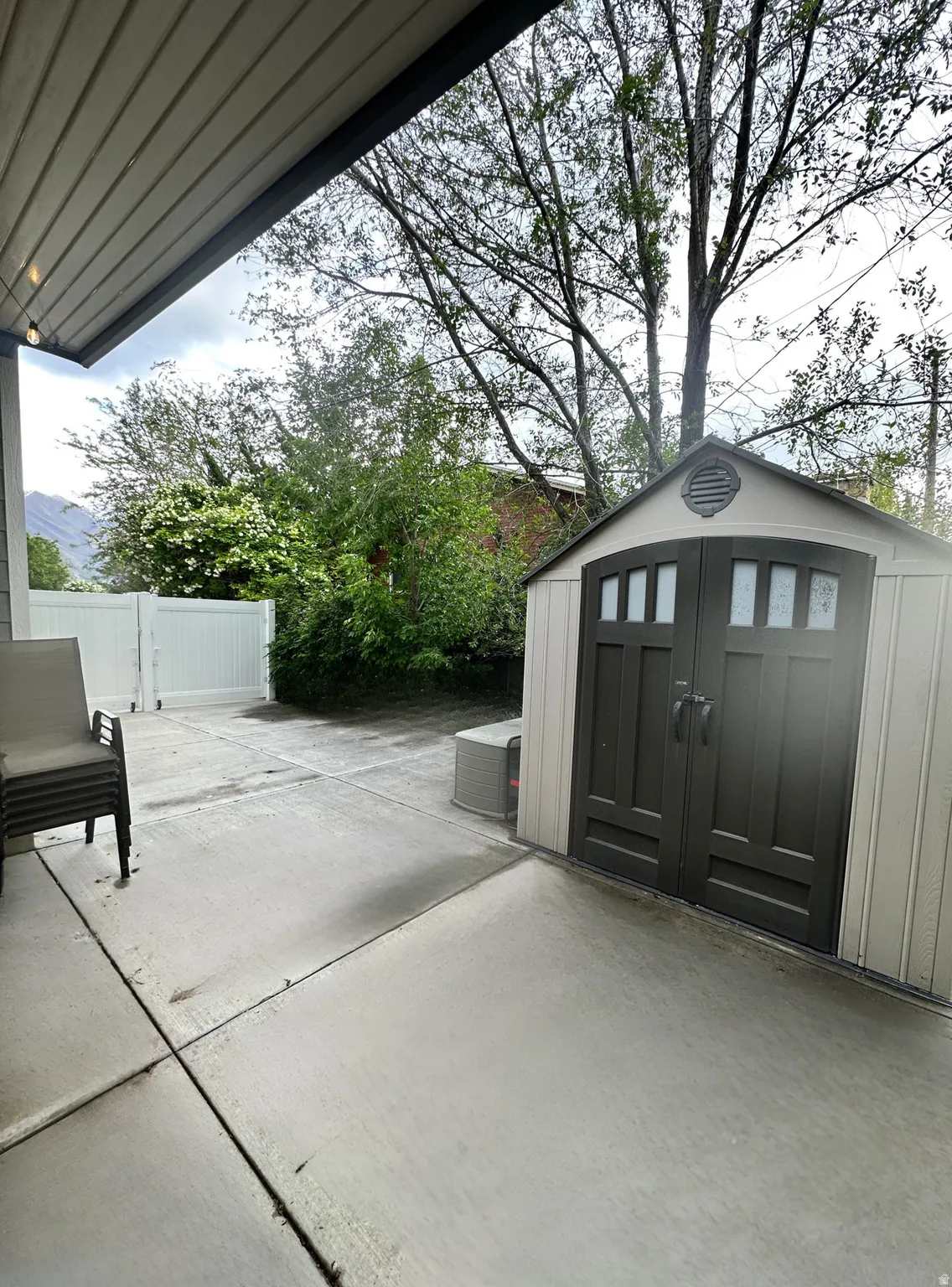 Exterior patio space featuring a concrete surface, white privacy fencing, and mature trees