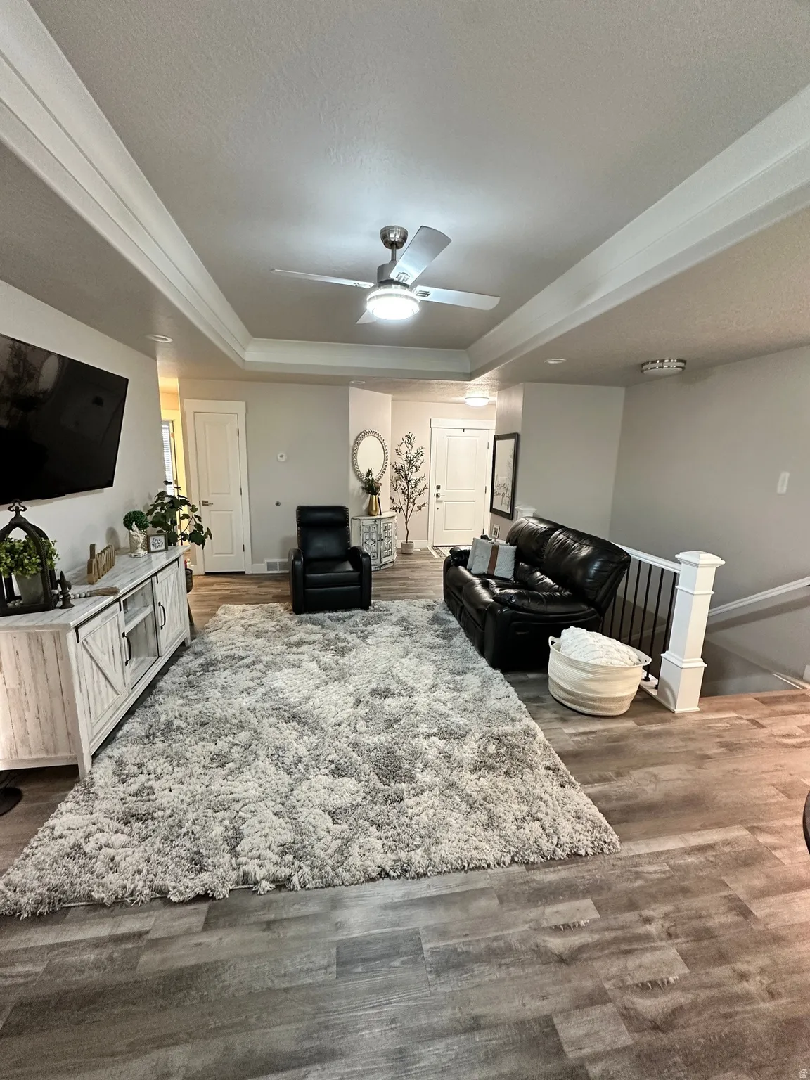 Spacious living area featuring wood-finish flooring, a tray ceiling with a modern ceiling fan, and light gray wall tones