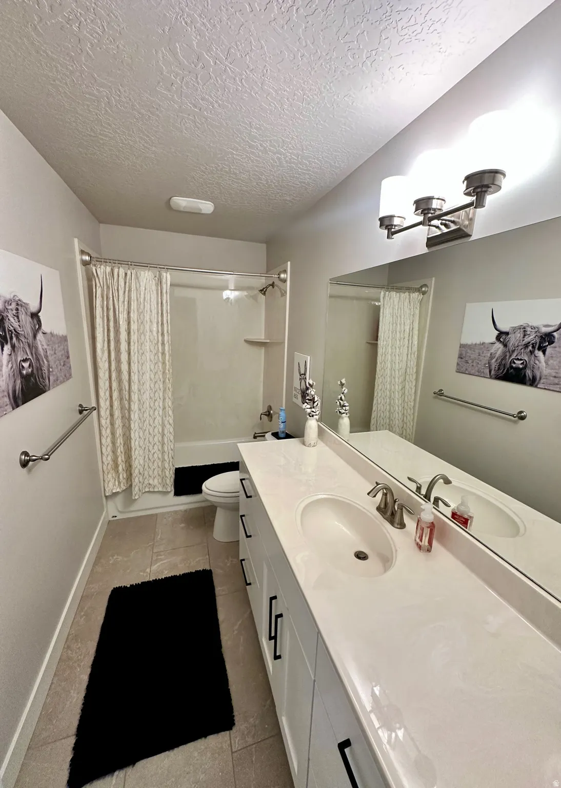Bathroom vanity featuring dual under-mount sinks, a light-toned countertop, and white cabinetry with matte black hardware