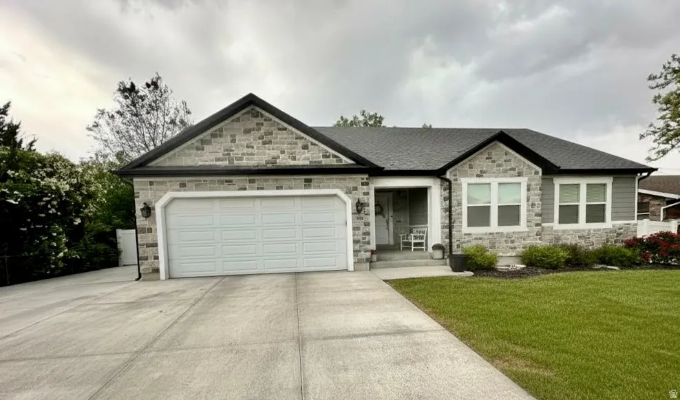 Stone and siding exterior featuring a two-car garage, concrete driveway, and front lawn