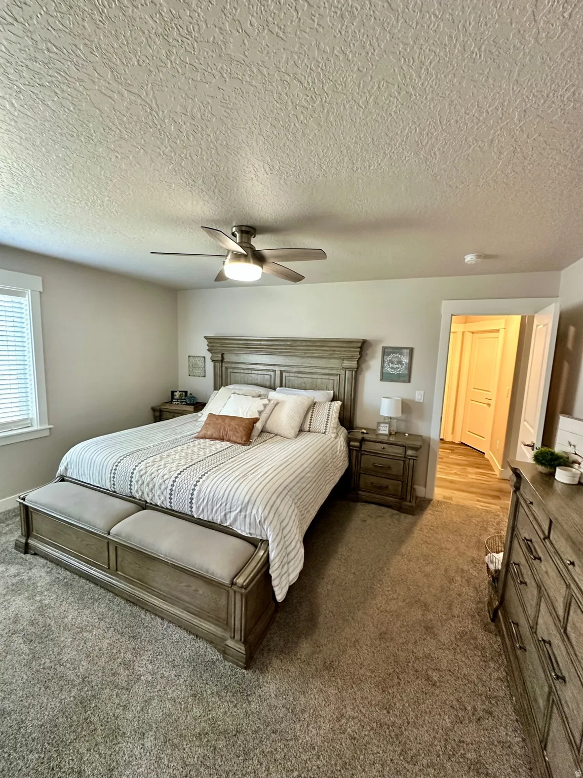 Spacious master bedroom featuring plush carpeting, a modern ceiling fan with integrated lighting, and a white-trimmed window with horizontal blinds