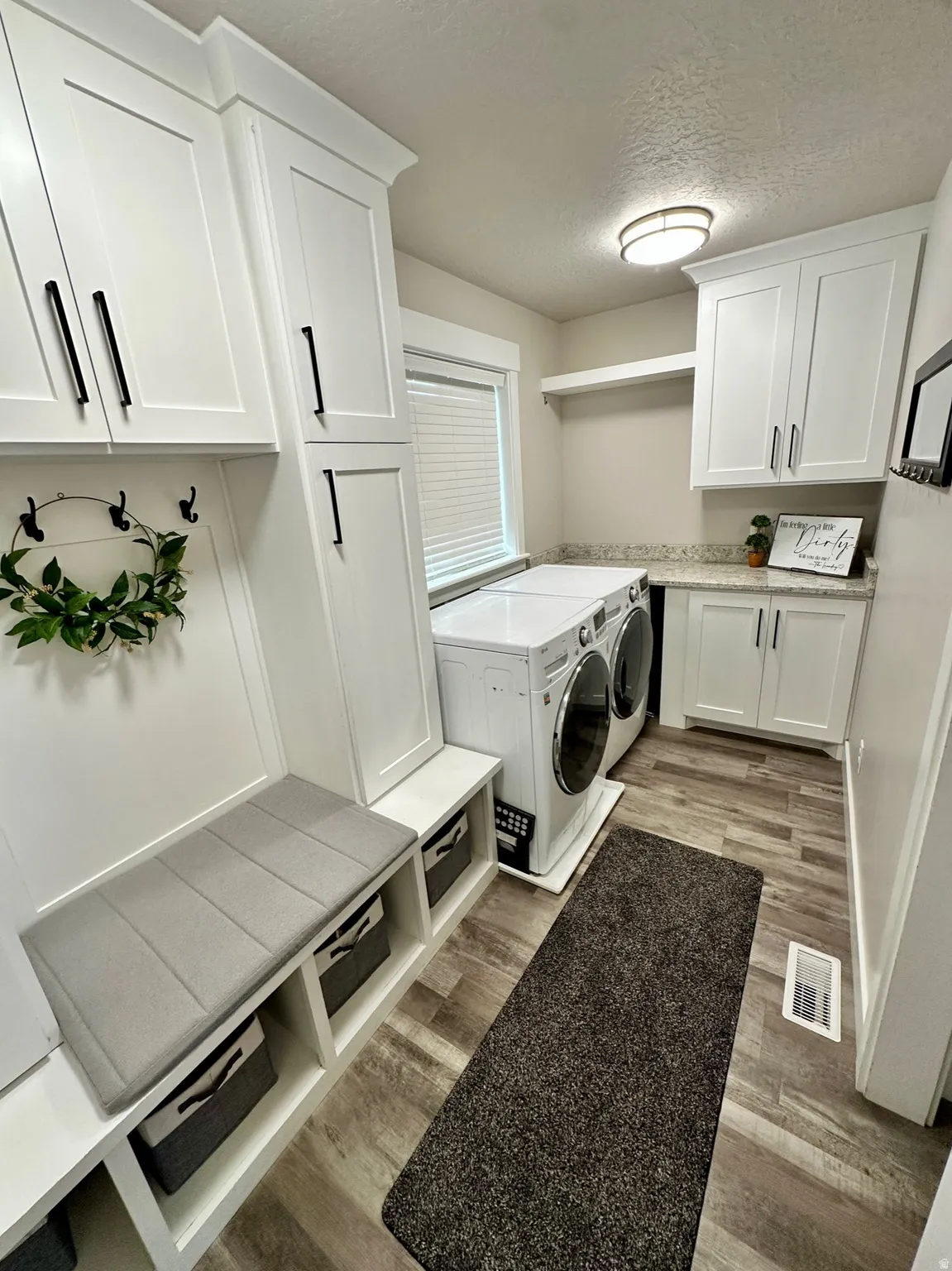 Dedicated laundry area featuring wood-finish flooring, white cabinetry with black hardware, and a built-in bench with open storage cubbies