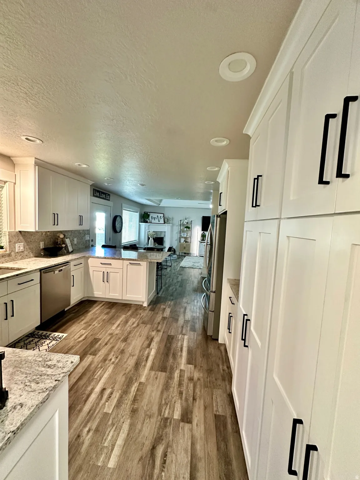 Kitchen featuring white shaker-style cabinetry with black hardware, stone countertops, wood-finish flooring, recessed lighting, and stainless steel appliances