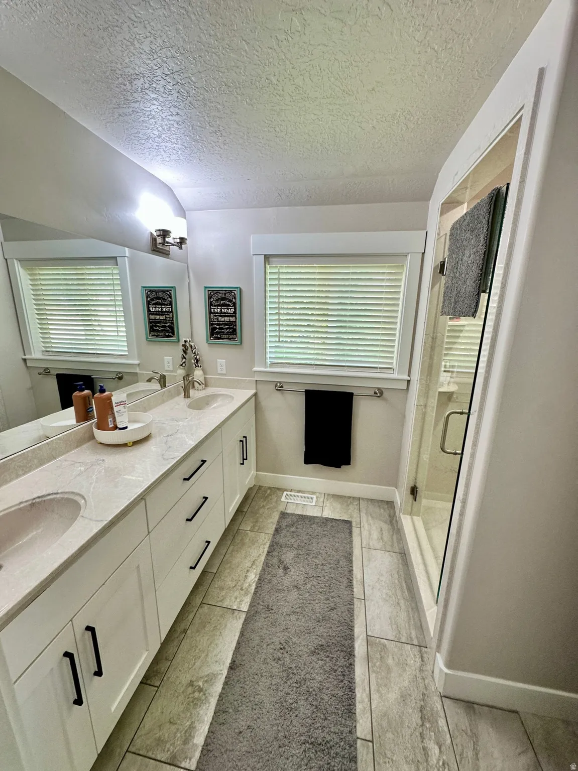 Master Bathroom featuring a double vanity with light-toned countertops, white cabinetry with dark hardware, and a framed mirror