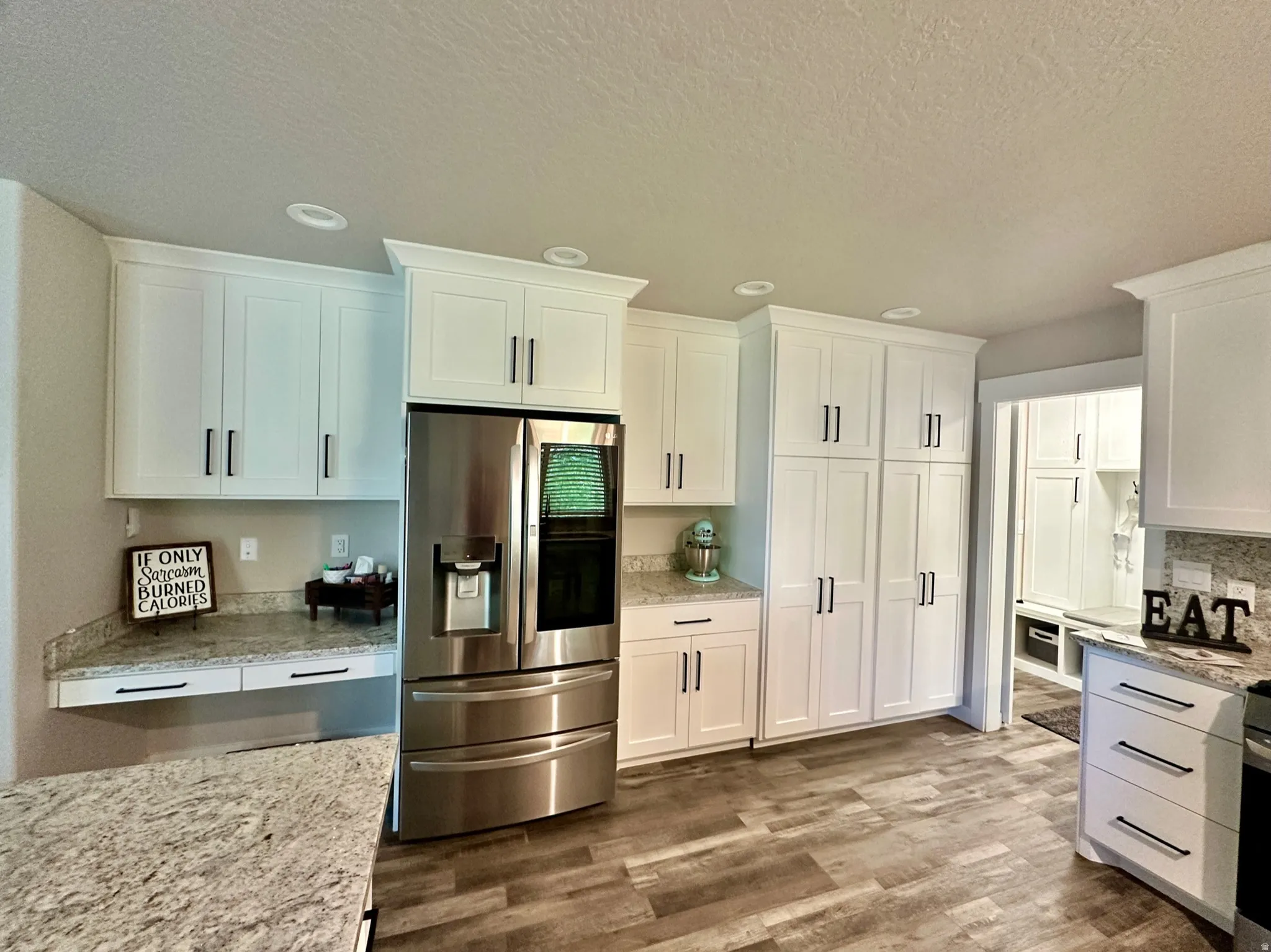 Kitchen featuring abundant white cabinetry with dark hardware, stainless steel refrigerator, granite-style countertops, wood-finish flooring, and recessed lighting