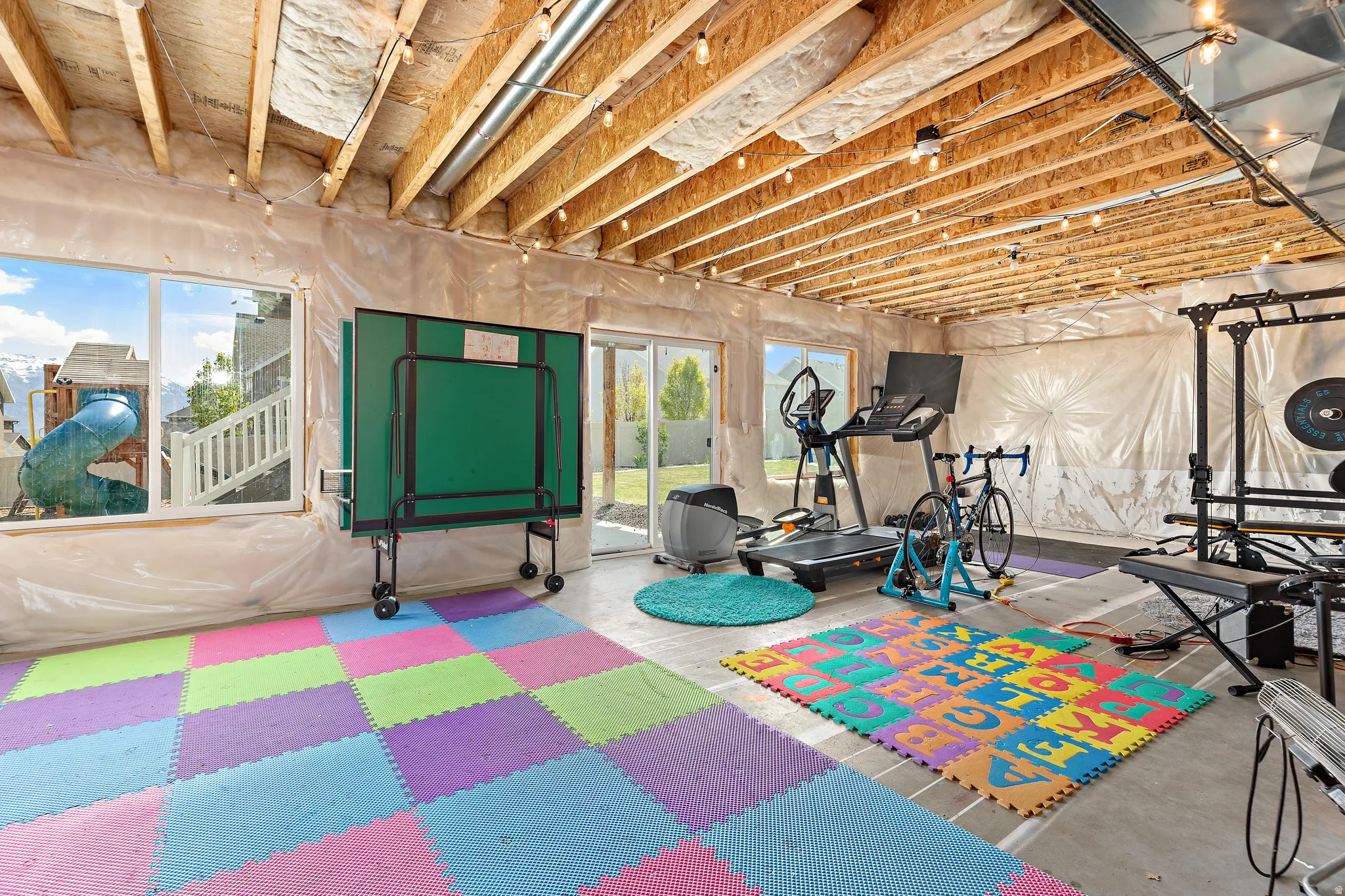 Daylight basement with exposed wood joist ceiling and string lighting