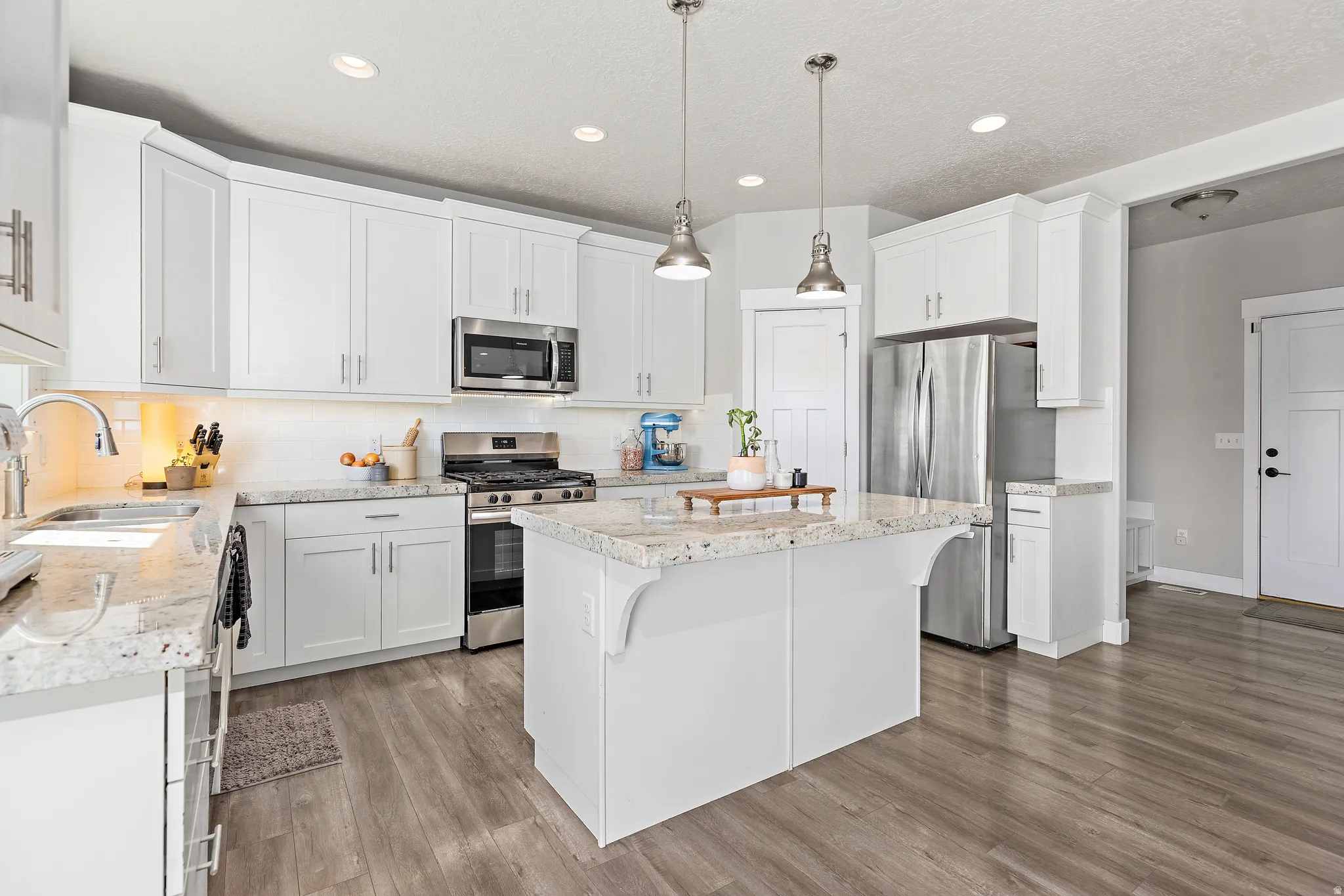 Modern kitchen featuring white cabinetry, stainless steel appliances, and a central island with a light-colored stone countertop