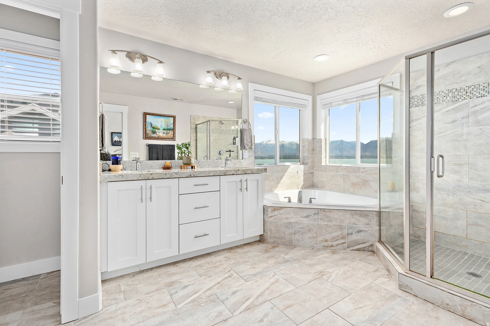 Spacious bathroom featuring a dual vanity with white cabinetry and light-toned countertops, a corner soaking tub, and a separate glass-enclosed shower