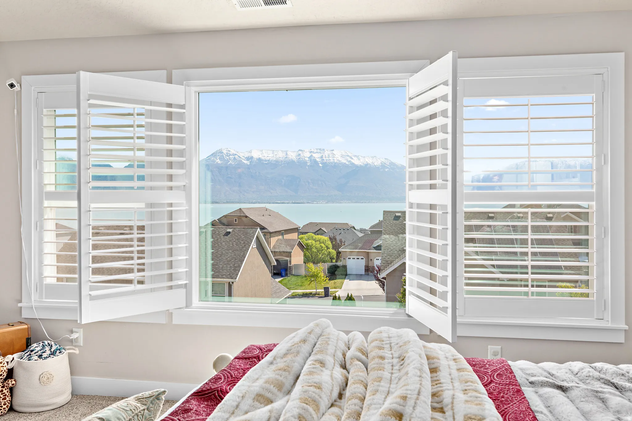 Multiple windows with white plantation shutters frame expansive mountain and water scenery