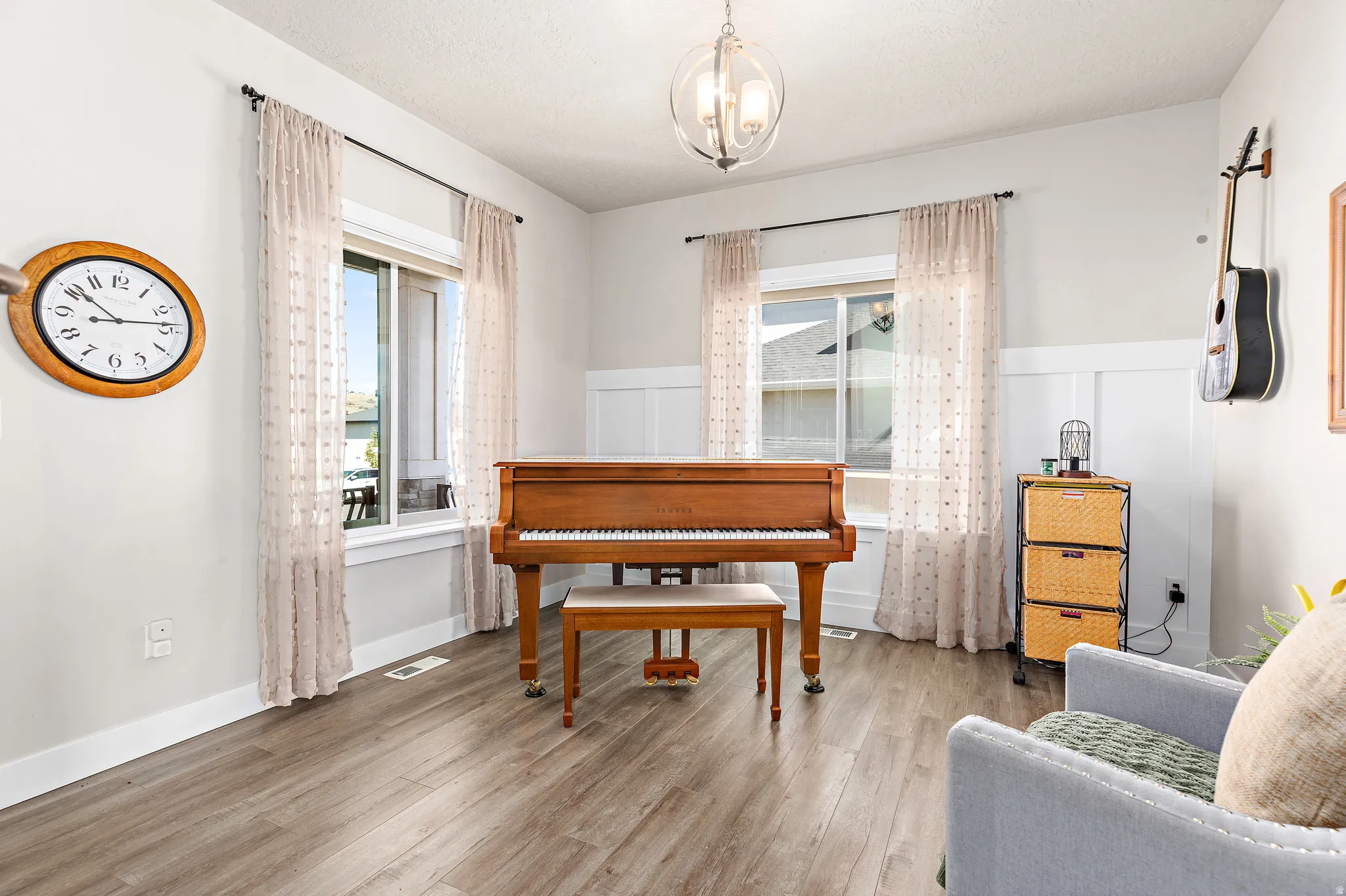 Spacious interior room featuring wood-finish flooring, white board and batten wall detailing, and multiple windows