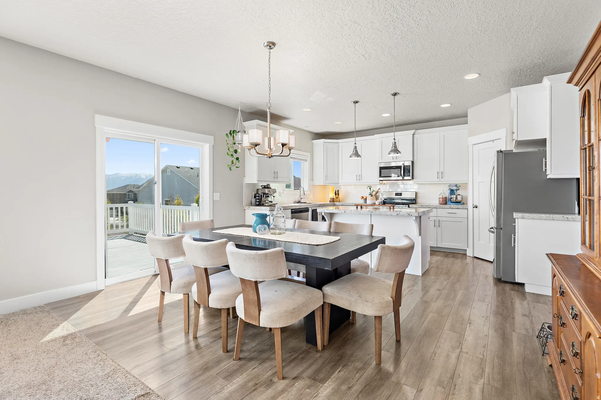 Open-concept dining area featuring wood-finish flooring, a contemporary chandelier, and direct access to an outdoor deck through a sliding glass door