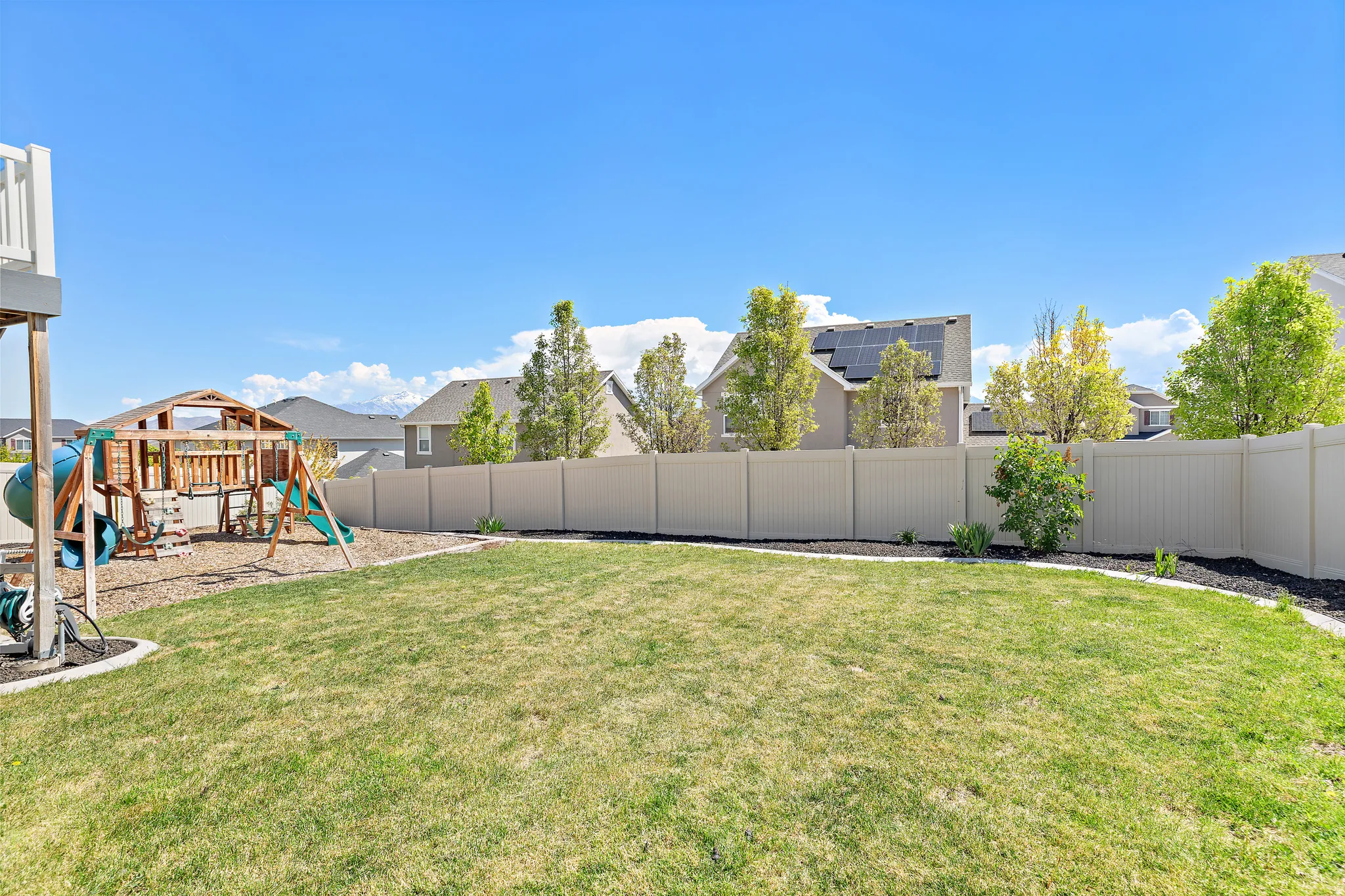 Spacious backyard featuring a manicured lawn, a full vinyl privacy fence, and mature trees along the perimeter