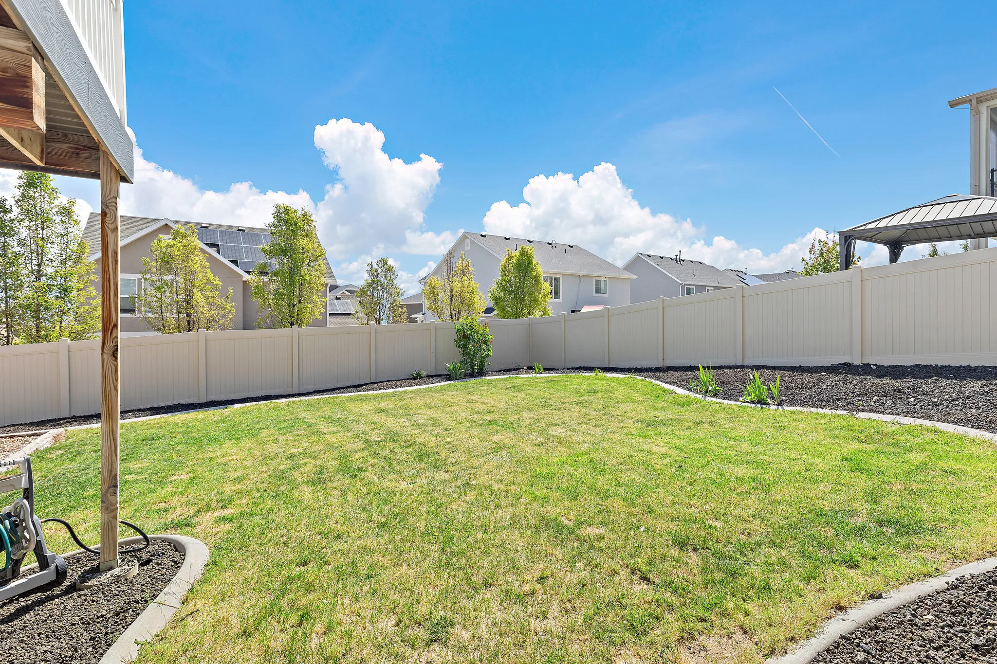 Expansive backyard featuring a manicured lawn, perimeter fencing, and decorative landscaping with dark mulch