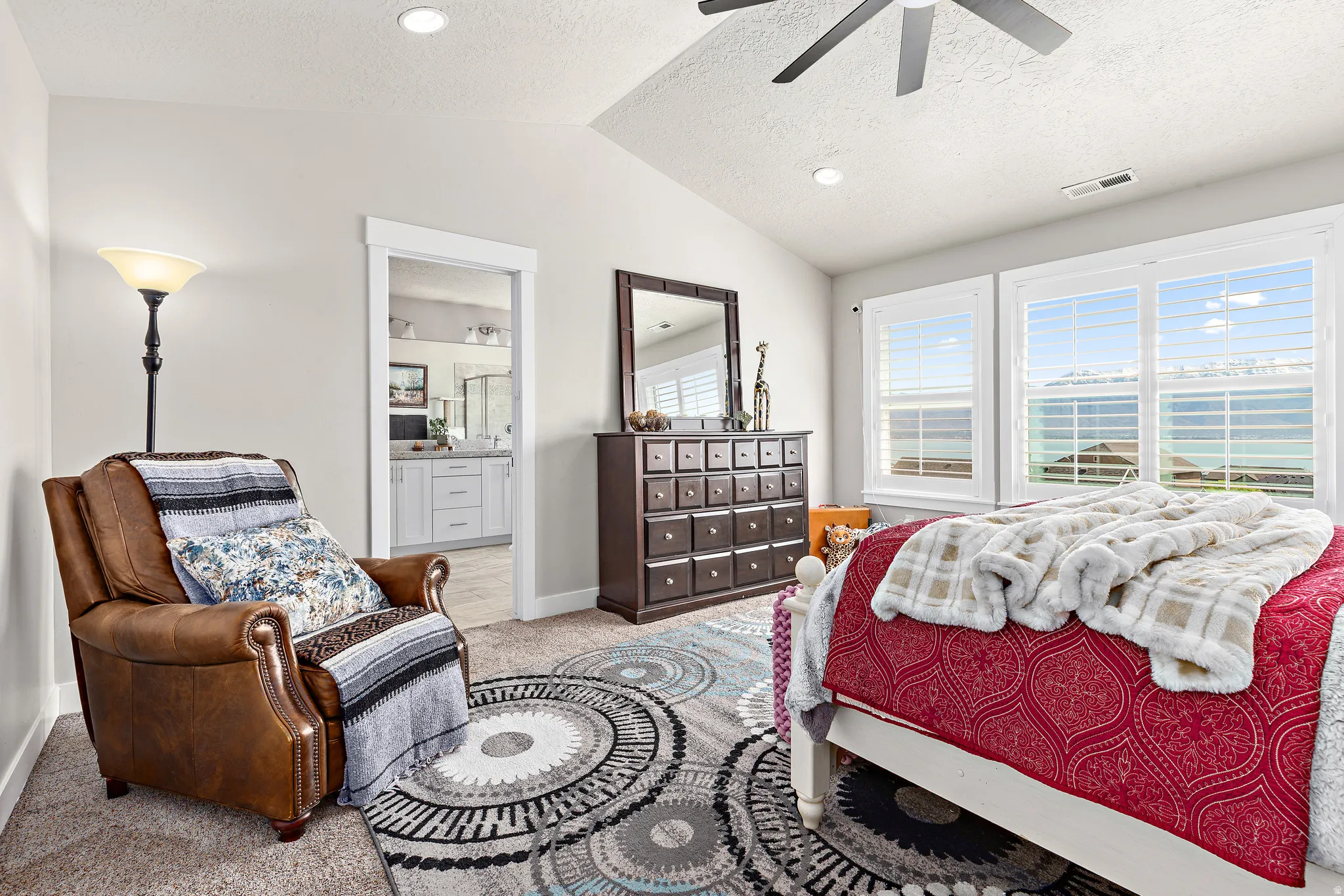 Spacious bedroom featuring vaulted ceilings, recessed lighting, a ceiling fan, and large windows with plantation shutters