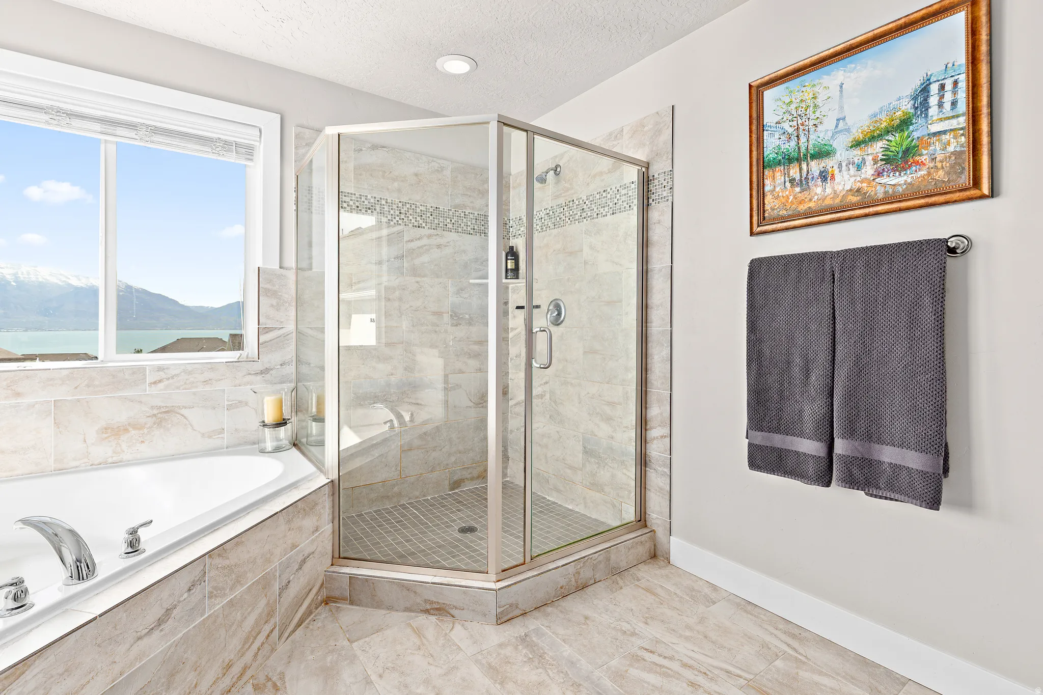 Bathroom featuring a corner soaking tub, glass-enclosed shower with a built-in bench, and large window with mountain and water backdrop