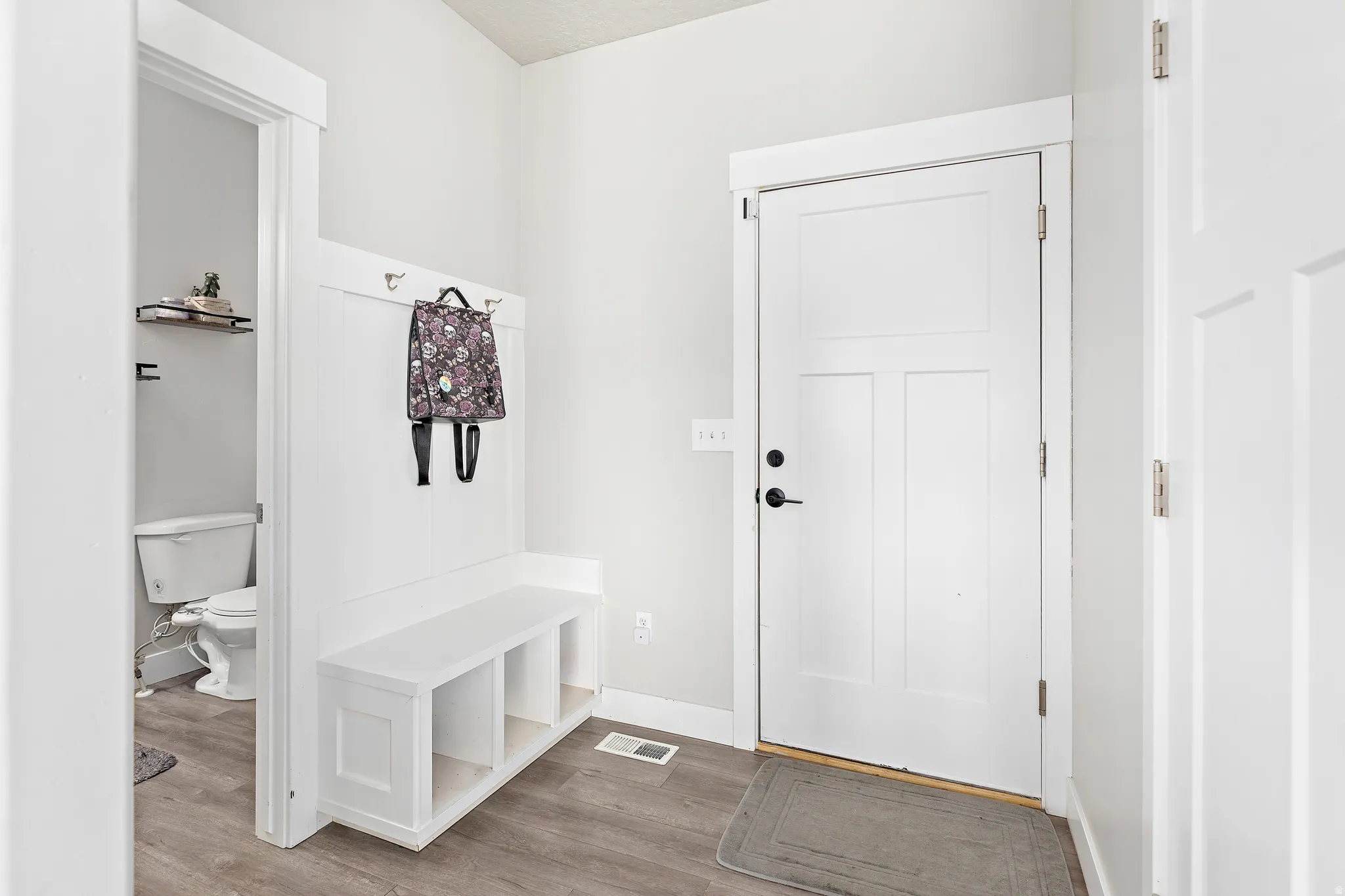 Entryway mudroom featuring a built-in bench with cubby storage, coat hooks, and wood-finish flooring
