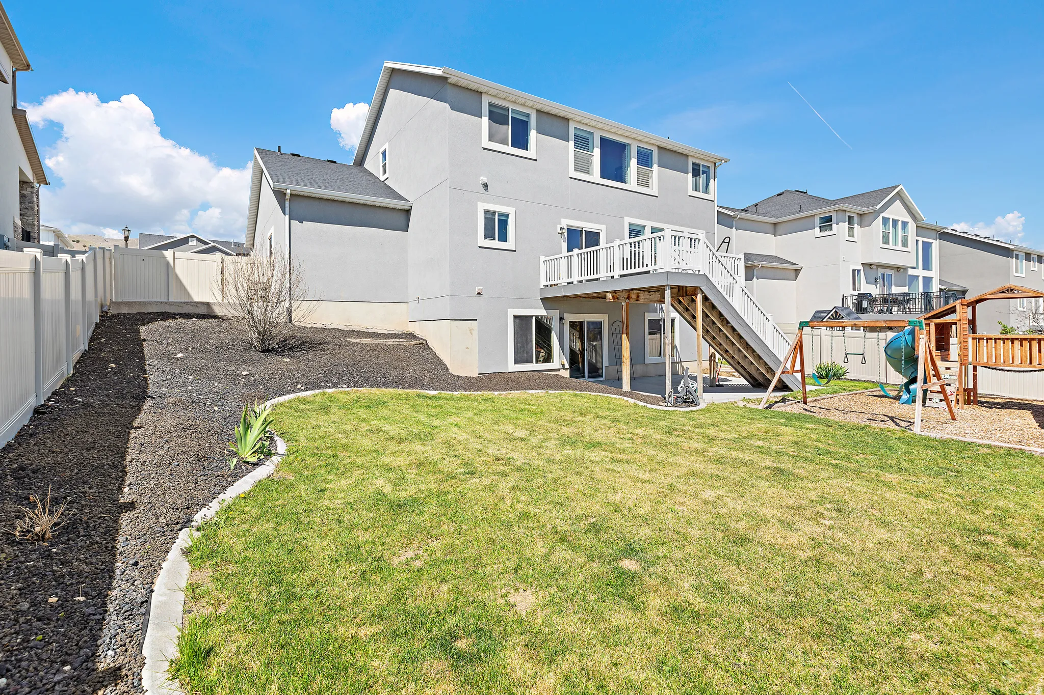 Expansive backyard featuring a manicured lawn, a raised deck with stairs, and a full-height privacy fence