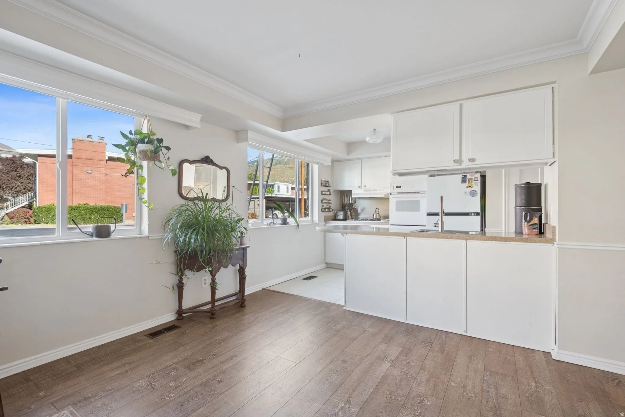 Kitchen with white cabinetry, white appliances, light wood-style flooring, a peninsula, and crown molding