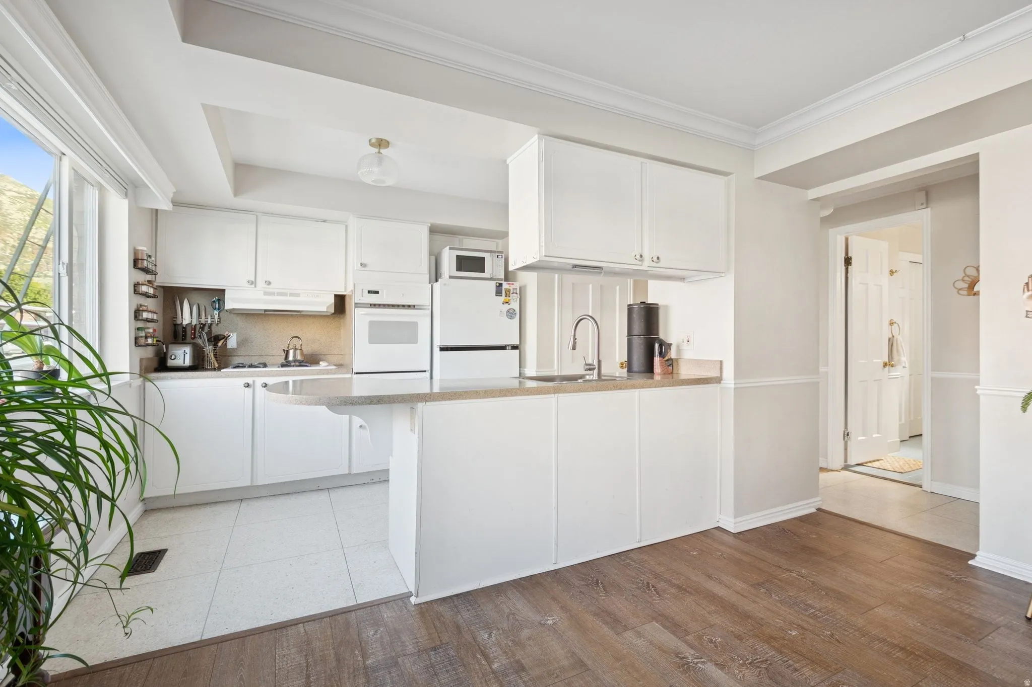 Kitchen featuring white cabinets, a peninsula, white appliances, and crown molding