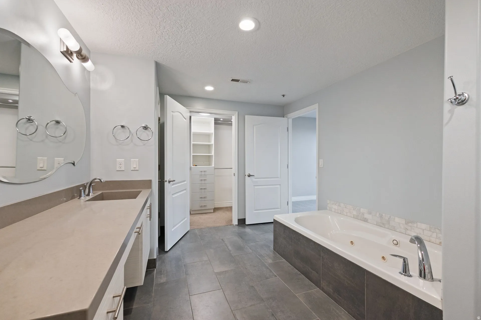 Bathroom featuring vanity, recessed lighting, a tub with jets, a walk in closet, and a textured ceiling