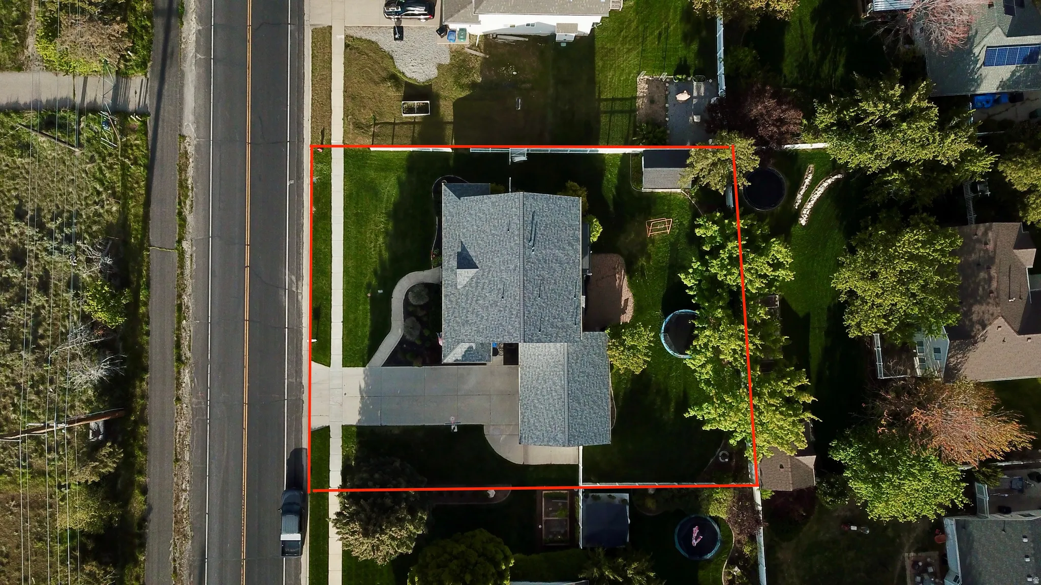Aerial overview showcasing the property's perimeter, a gray-shingled roof, a paved driveway, and a spacious green lawn