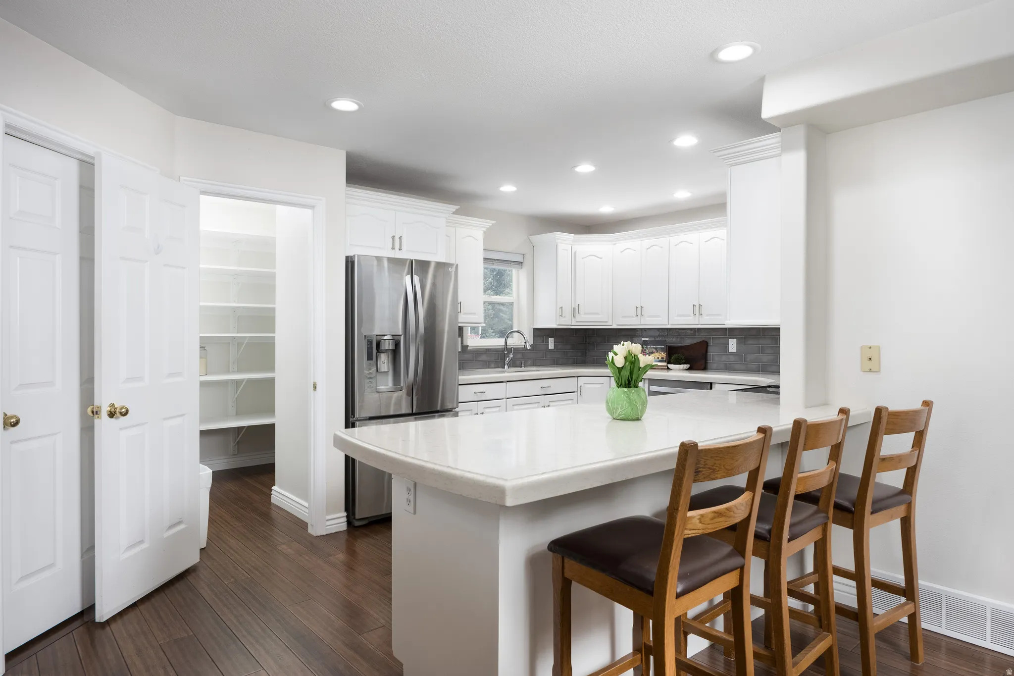 White kitchen cabinetry with stainless steel appliances, a white countertop island, and dark wood-finish flooring
