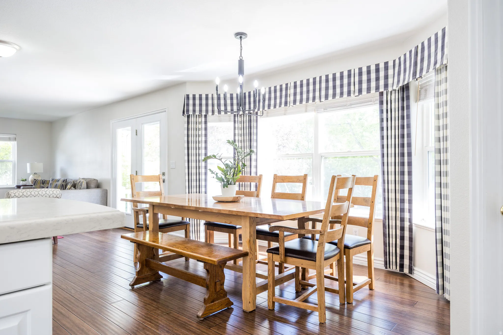 Dining area featuring rich wood-finish flooring, a contemporary chandelier, a bay window with plaid valances, and light-filled French doors