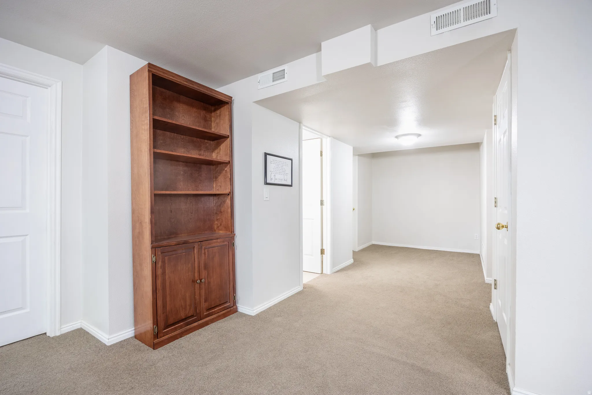 Carpeted room featuring a built-in wood cabinet with open shelving and lower storage, white walls, and a flush-mount ceiling light fixture
