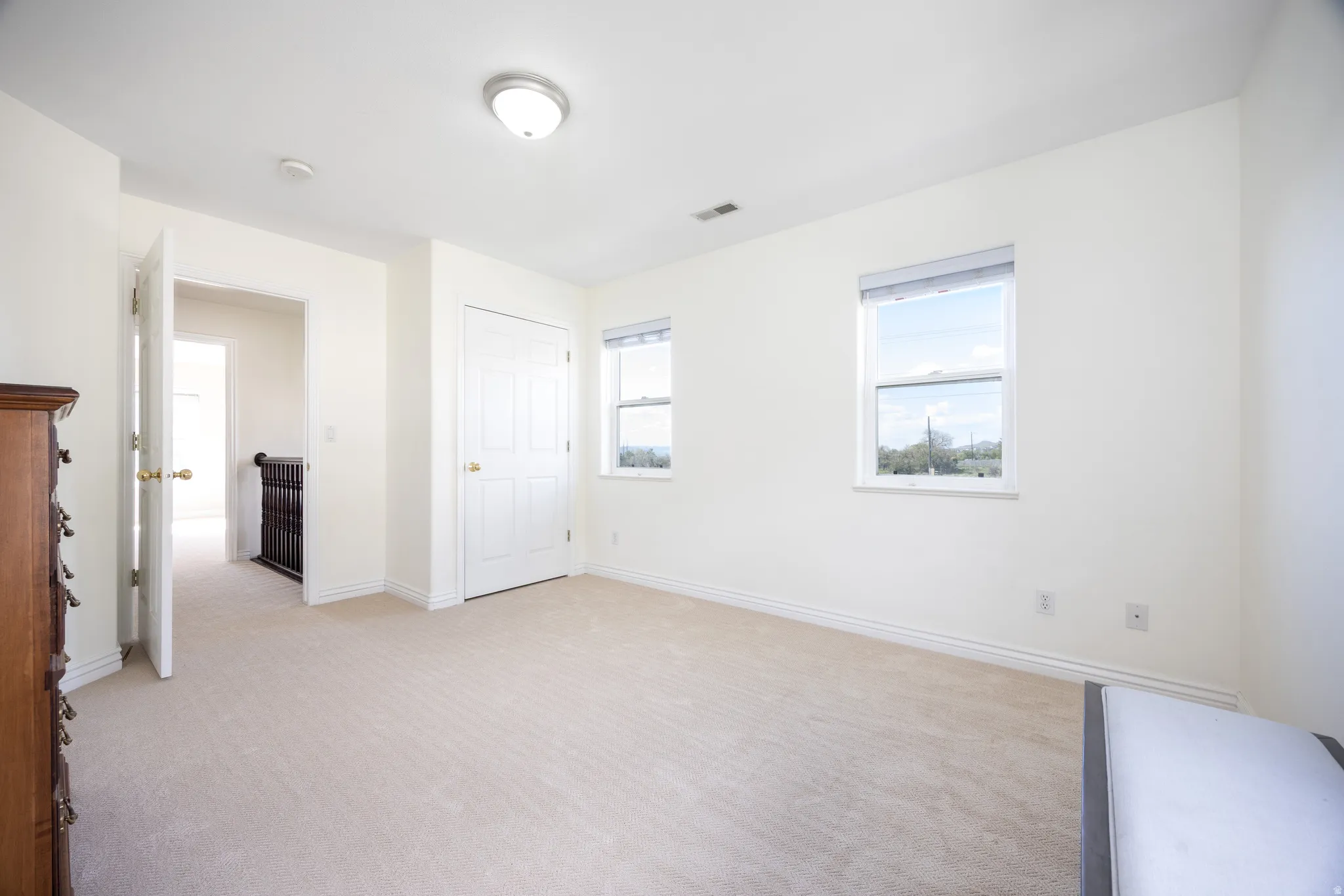 Carpeted room with two double-hung windows, a flush-mount ceiling light, a white paneled door, and white baseboards