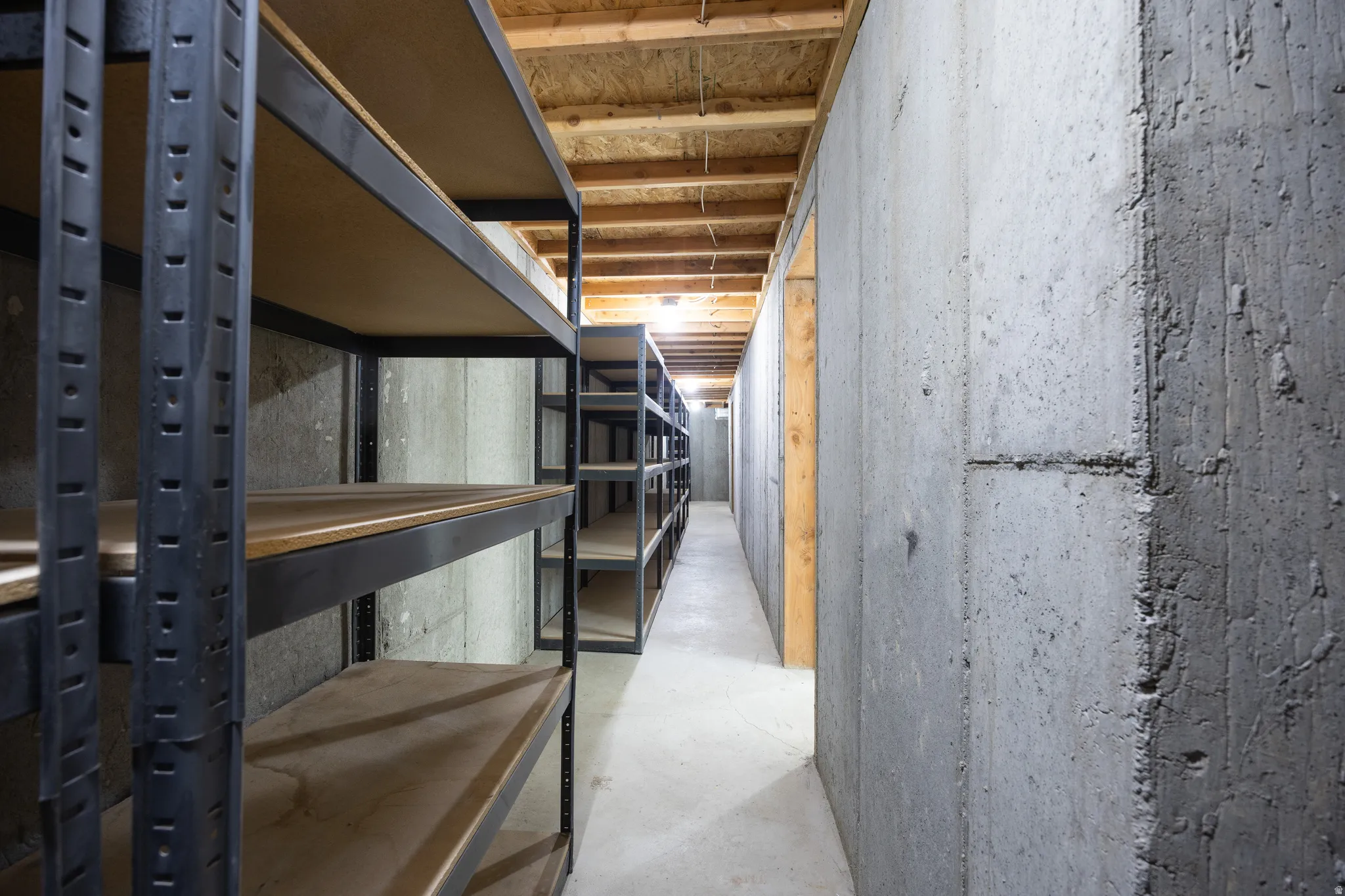 Basement storage area featuring extensive metal shelving, exposed concrete walls, an unfinished wood ceiling, and concrete flooring