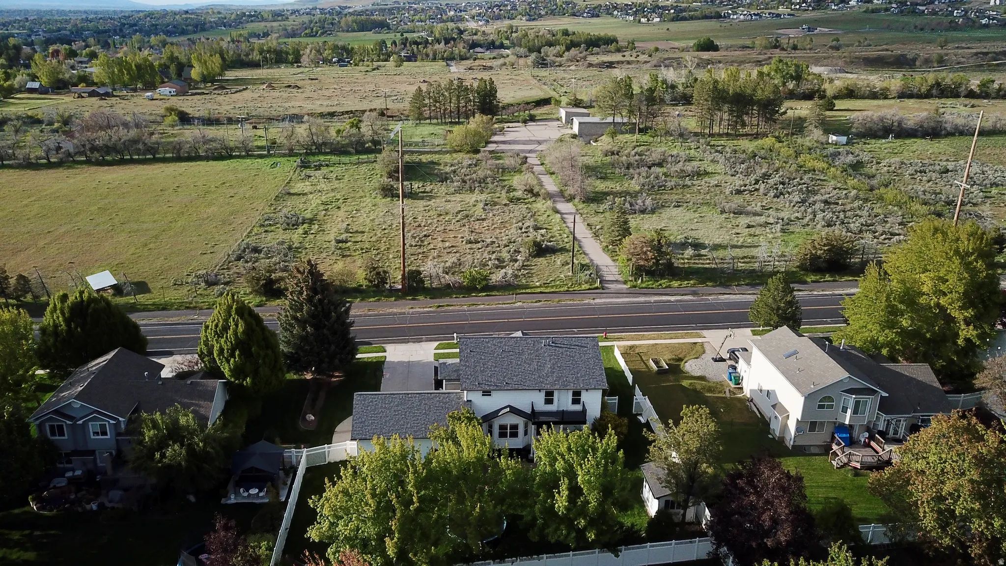 Aerial view showcasing a residential property with a multi-level exterior, dark shingle roofing, and mature perimeter trees