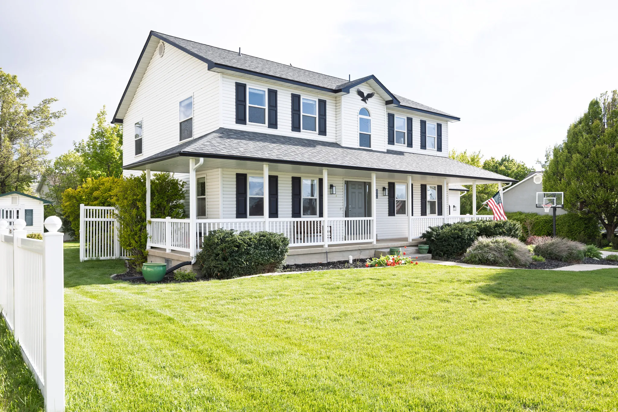 Two-story home featuring a full-width covered porch, white vinyl siding, dark shutters, and a well-maintained front lawn