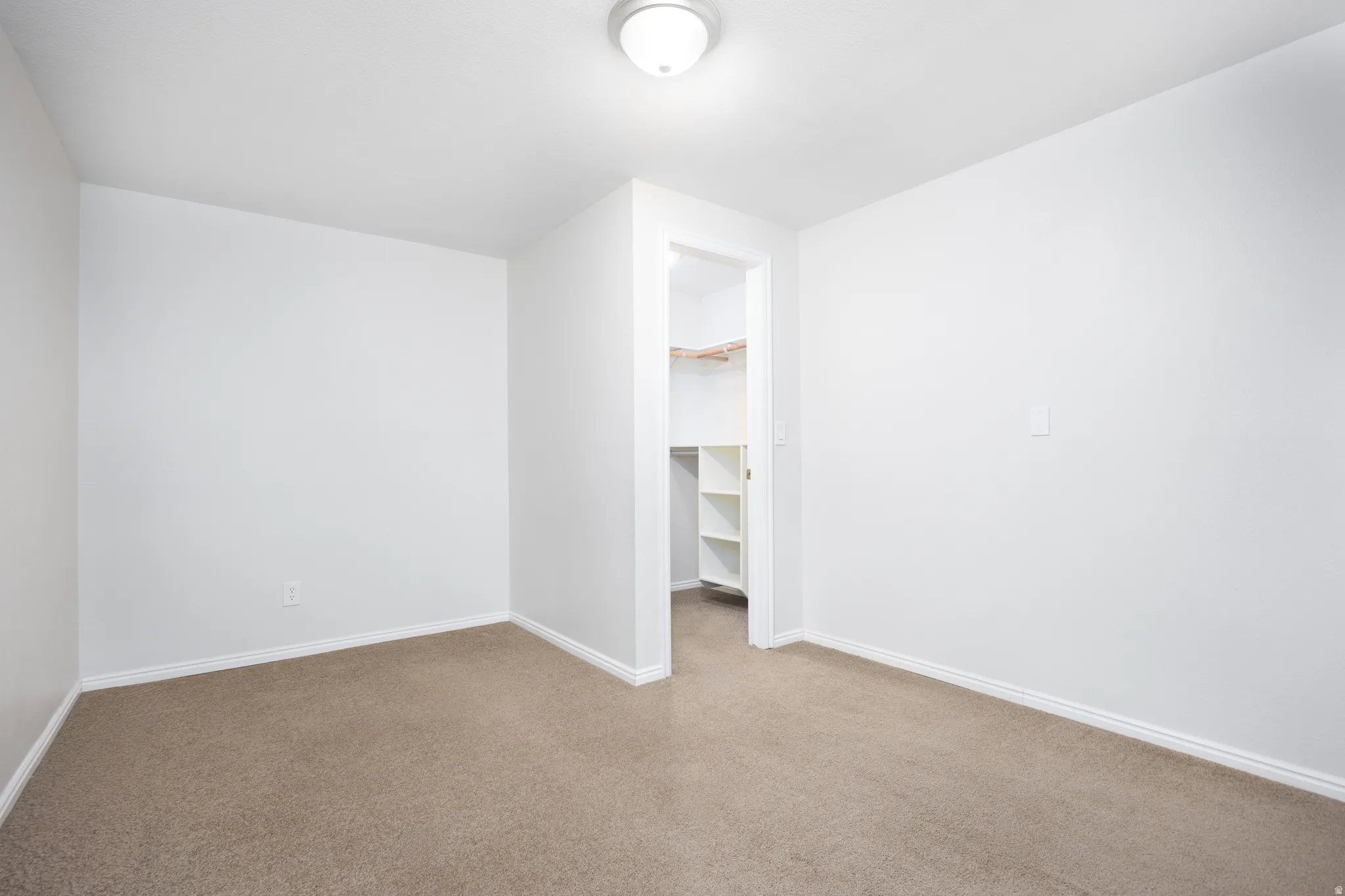 Neutral-toned room featuring light beige carpeting, white baseboards, and a flush mount ceiling light fixture