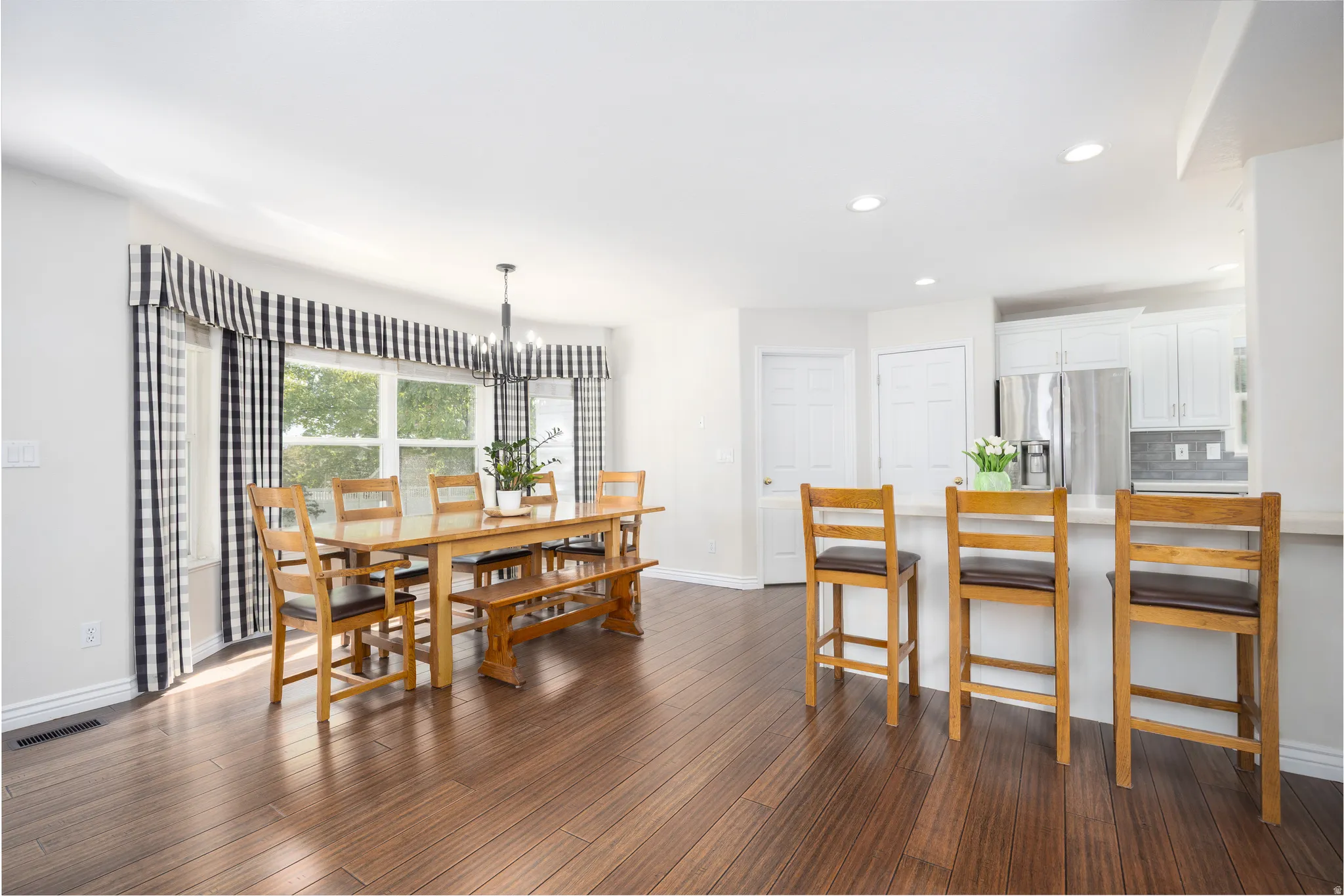 Open-concept dining area featuring wood-finish flooring, a bay window, and a contemporary chandelier