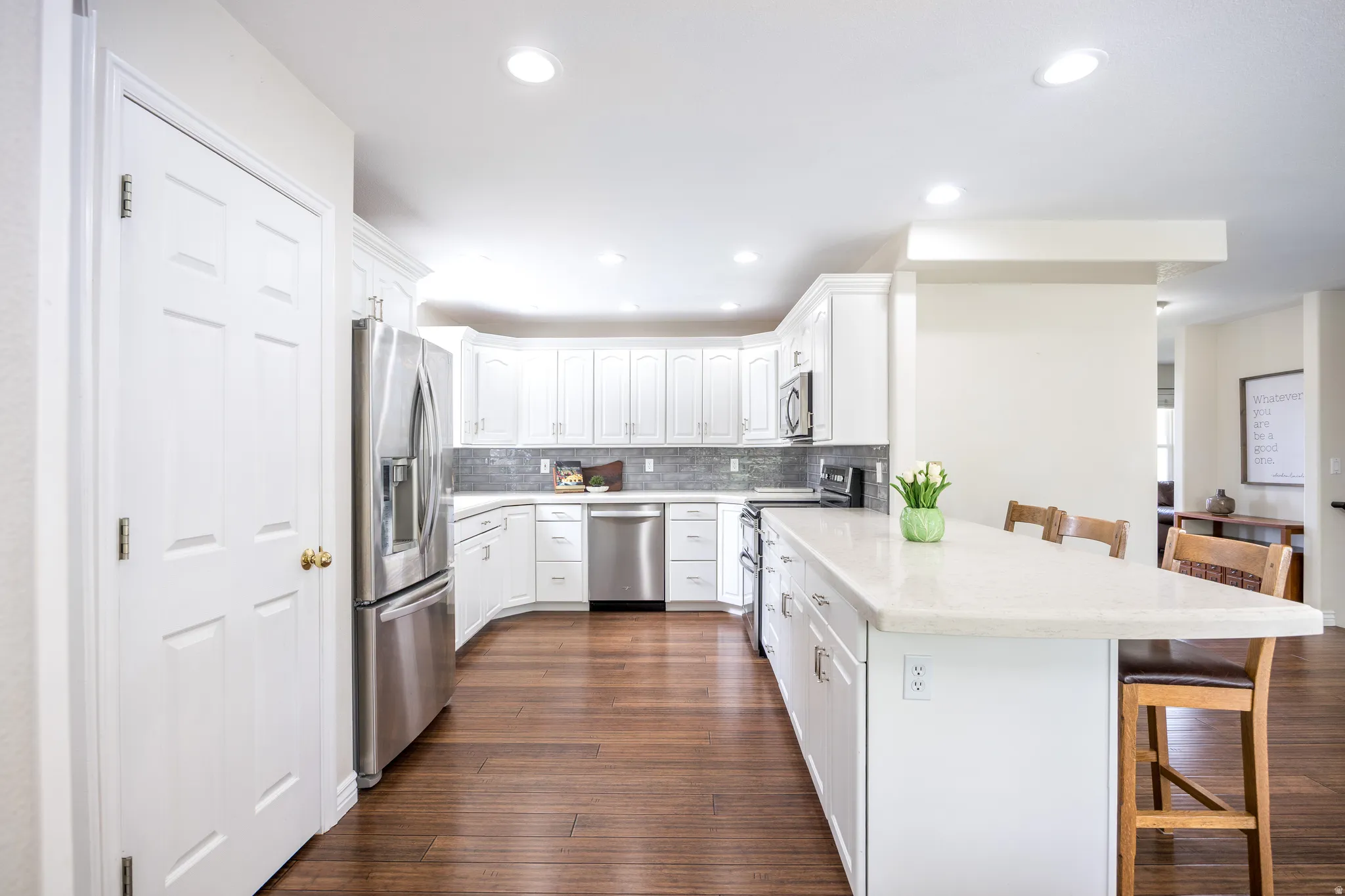 Modern kitchen featuring white cabinetry, stainless steel appliances, a tile backsplash, and wood-finish flooring