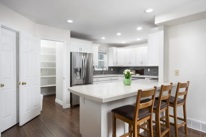 White kitchen cabinetry with stainless steel appliances, a white countertop island, and dark wood-finish flooring