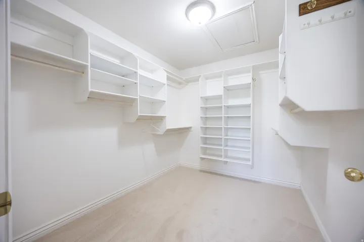 Spacious closet featuring white built-in shelving, multiple hanging rods, and neutral-toned carpeting
