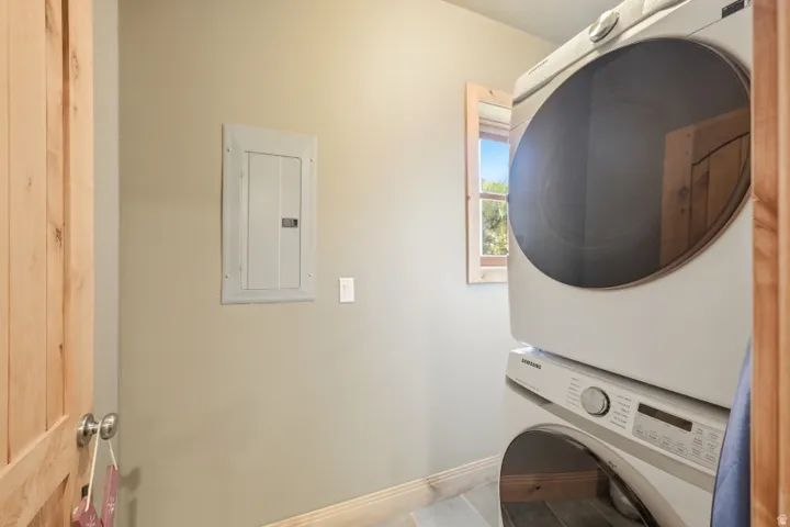 Laundry room with electric panel, stacked washer and dryer, and light tile patterned floors