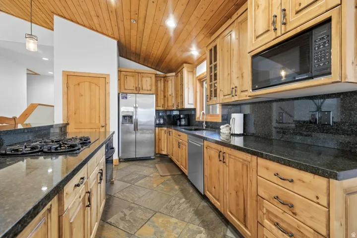 Kitchen with black appliances, dark stone countertops, a vaulted wood ceiling, hanging light fixtures, and backsplash