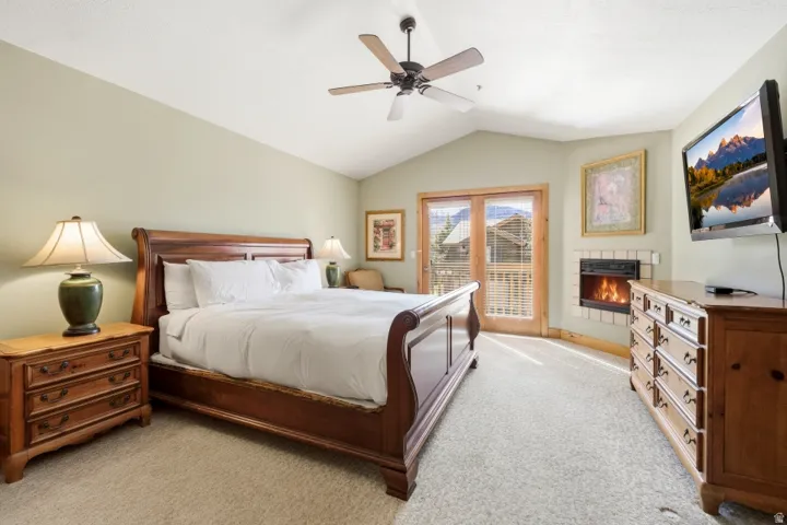 Bedroom featuring light colored carpet, ceiling fan, access to exterior, and a fireplace