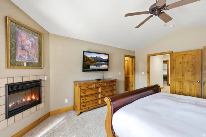 Bedroom with a fireplace, light carpet, vaulted ceiling, and a ceiling fan