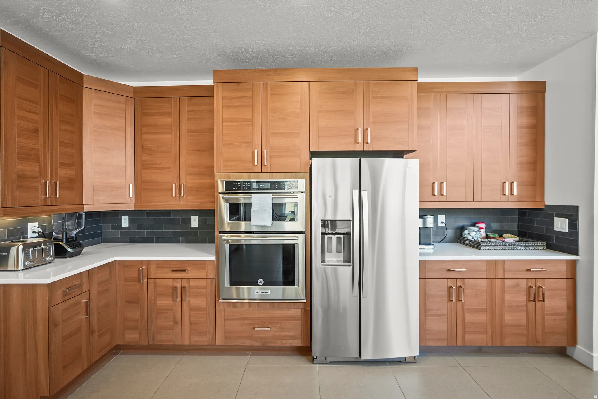 Kitchen with stainless steel appliances, backsplash, a textured ceiling, and wood finish cabinets