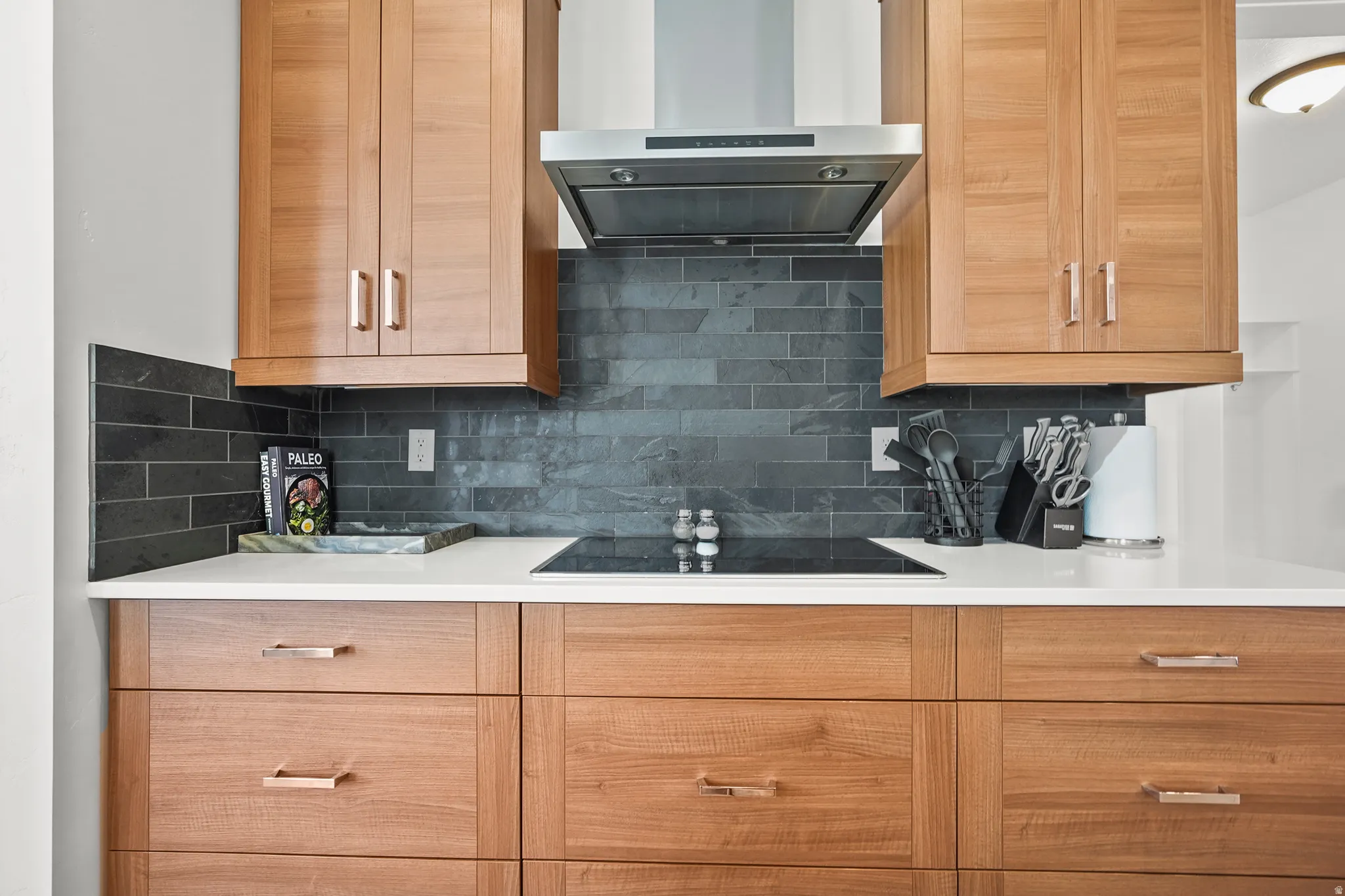 Kitchen with decorative backsplash, black electric stovetop, and light stone countertops