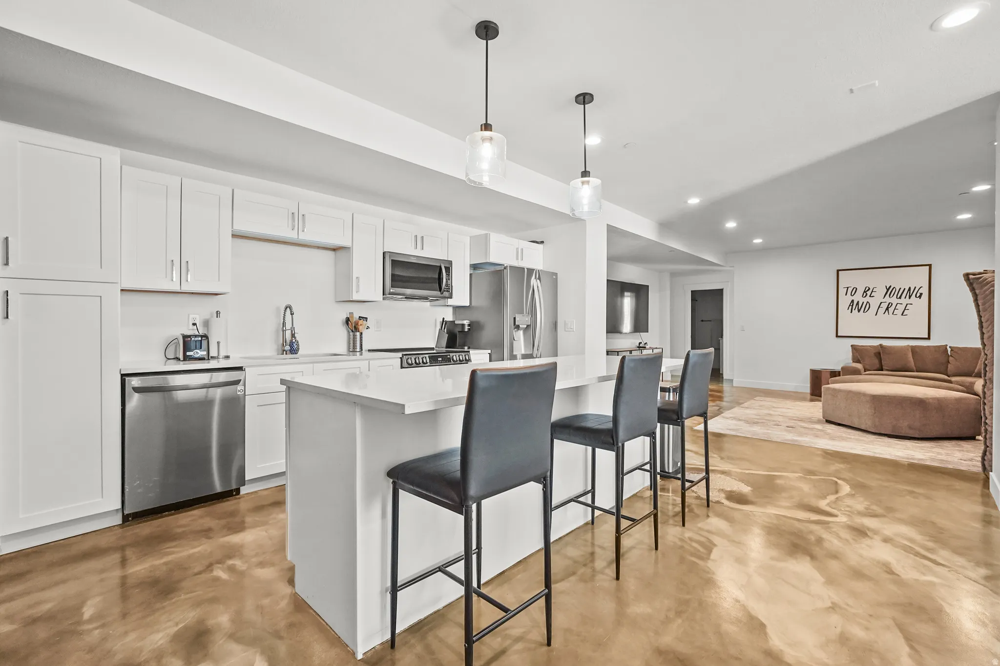 Kitchen with concrete floors, open floor plan, a center island, a breakfast bar area, and white cabinets