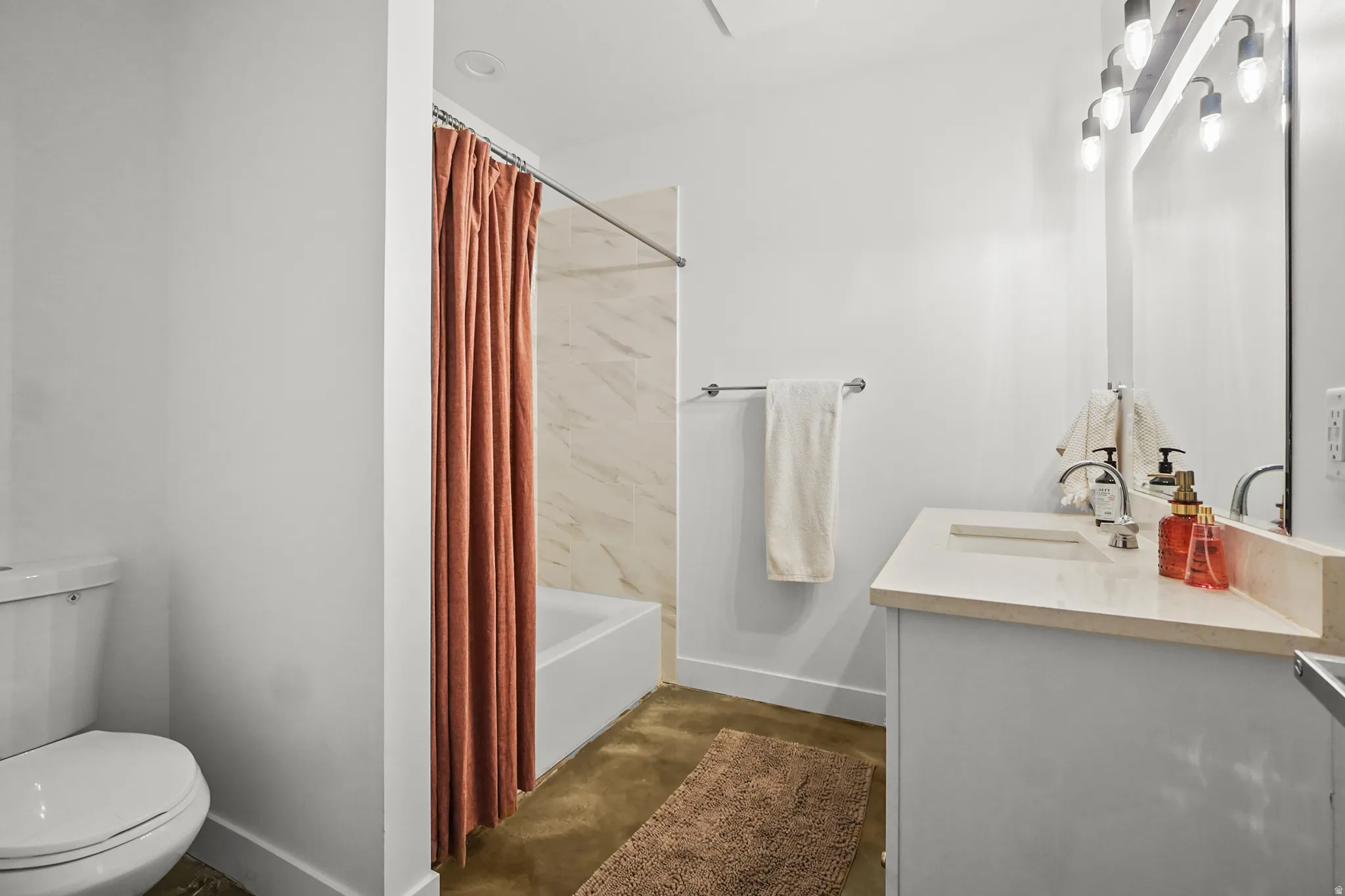 Bathroom with vanity, shower / tub combo, and concrete flooring