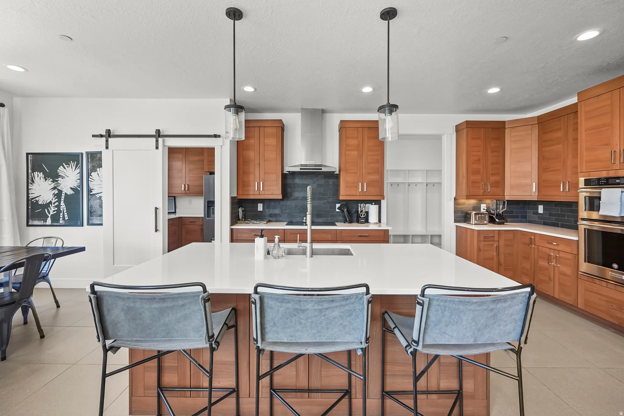 Kitchen featuring a barn door, wood finish cabinets, an island with sink, and pendant lighting