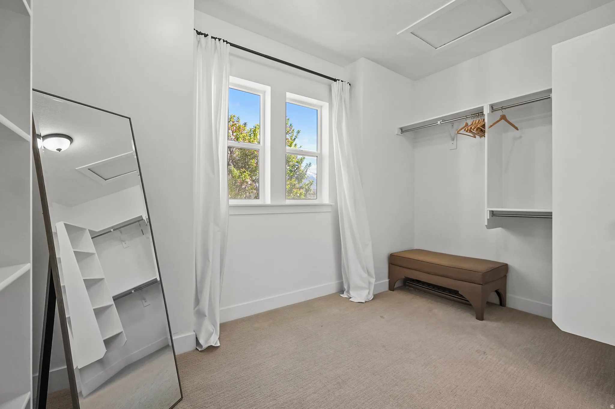 Walk in closet with attic access and light colored carpet