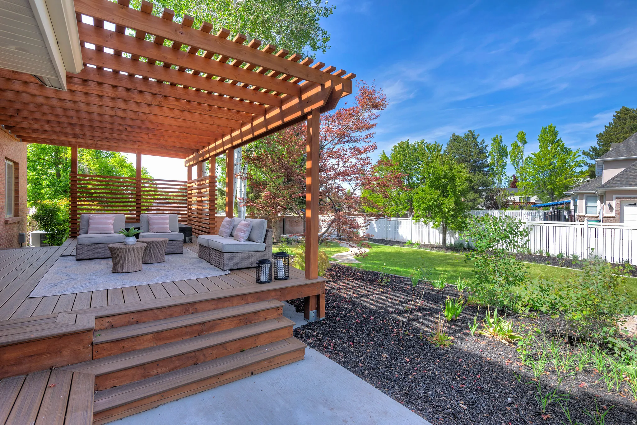 Fully fenced backyard featuring outdoor seating, a pergola, and a private deck with garden beds.